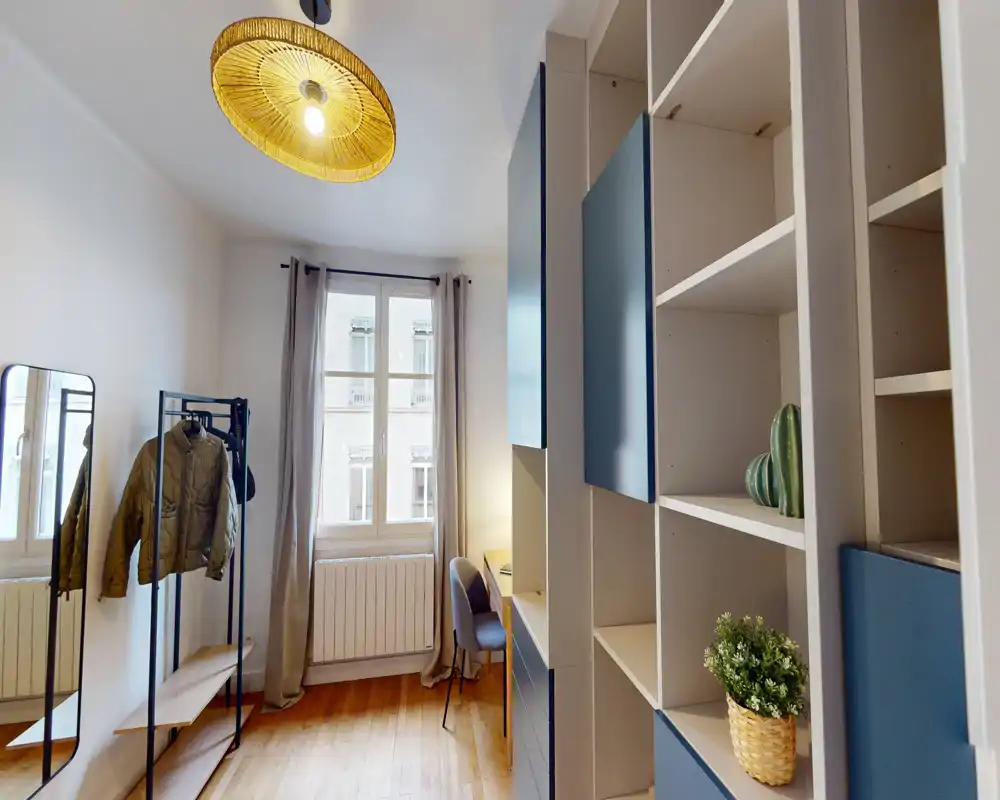 Bright, modern bedroom-studio with built-in shelving, a clothes rack, desk by the window and warm wooden floors; the bed is not visible in this shot.
