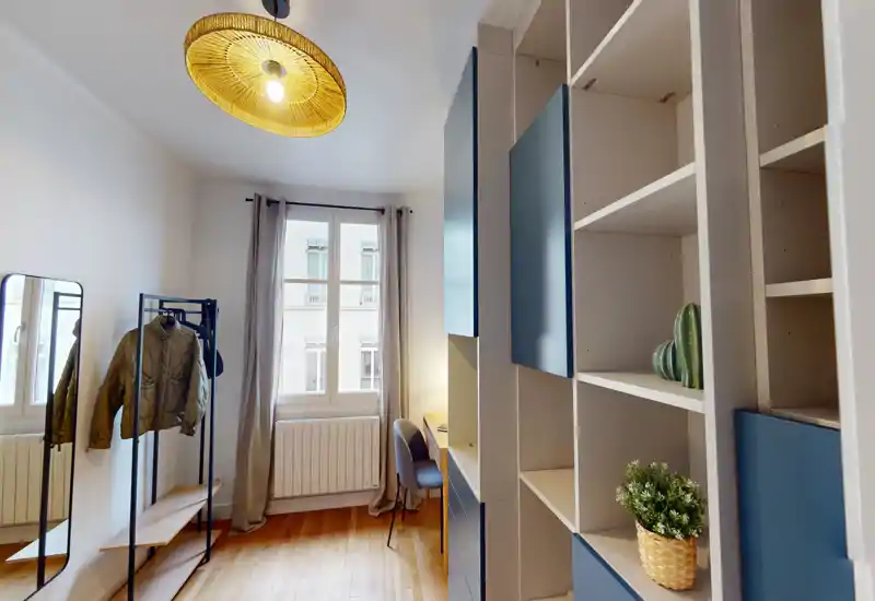 Bright, modern bedroom-studio with built-in shelving, a clothes rack, desk by the window and warm wooden floors; the bed is not visible in this shot.