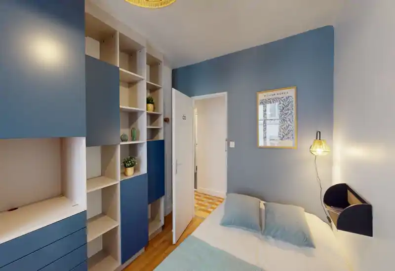 Compact, styled bedroom with a double bed, soft blue accents and built-in shelving; bright and welcoming for short stays.