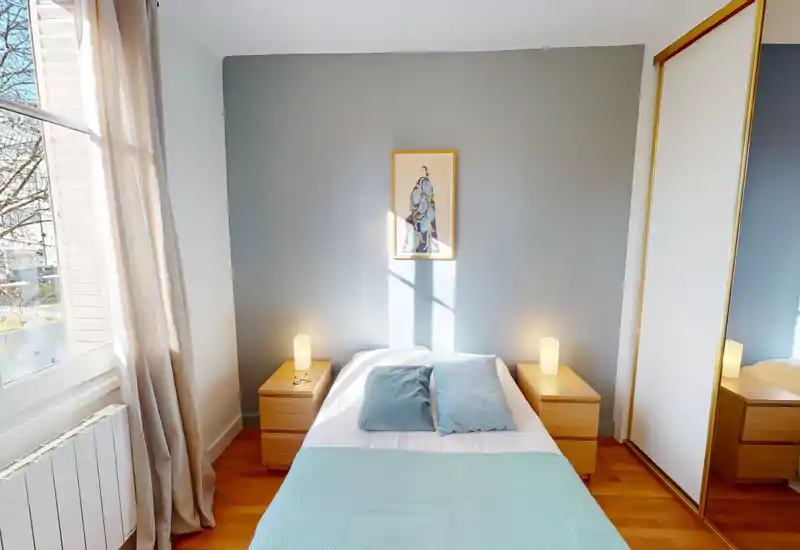 Bright, stylish bedroom with a centrally placed double bed, matching bedside tables and lamps, and a large window providing natural light.