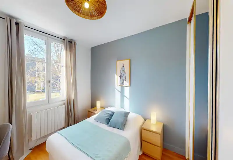 Bright, well-styled bedroom with a neatly made double bed, bedside tables and soft natural light from a large window.