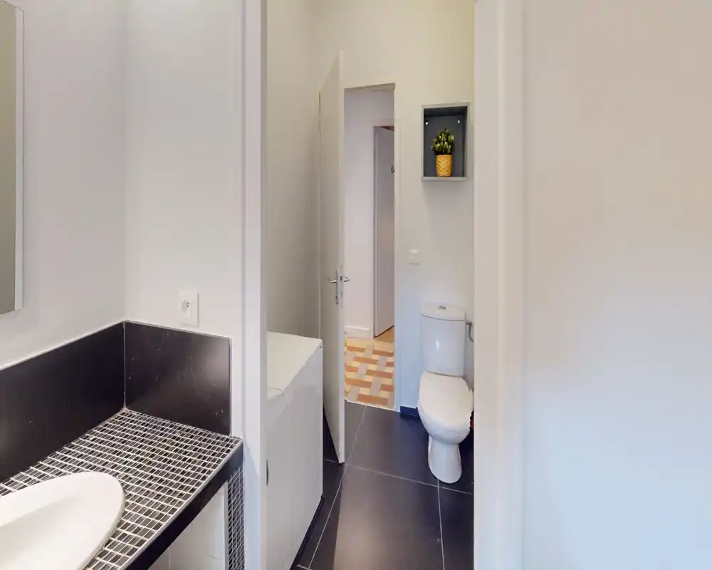 Compact, modern bathroom with a toilet, sink and tiled counter. Clean lines, dark floor tiles and neutral walls create a neat, functional space.