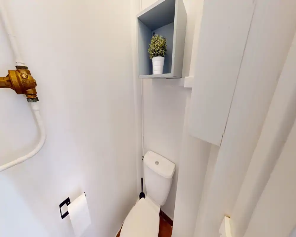 Compact bathroom with a white toilet, wall-mounted shelf and toilet brush; clean, well-lit small WC ideal for a short-stay listing.