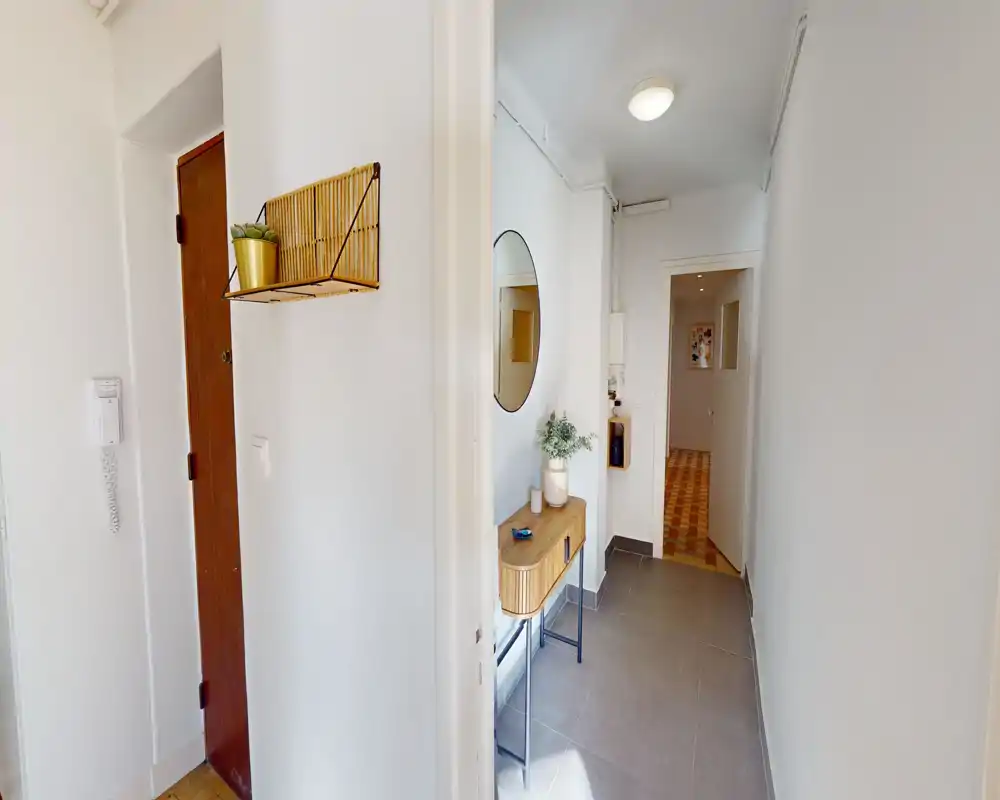 Bright, modern entrance hallway with a small console table, round wall mirror and decorative plants, leading to inner rooms.
