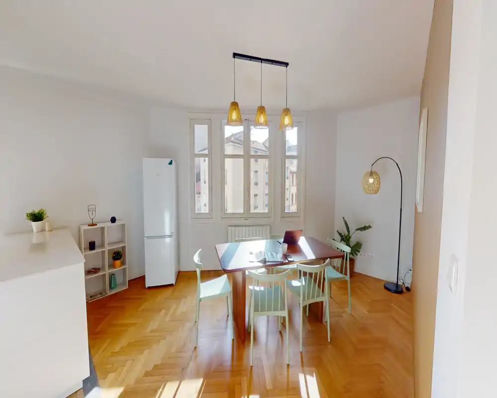 Bright, stylish dining area with a wooden table, four chairs and large windows that flood the space with natural light. Warm parquet floor and pendant lights create an inviting atmosphere for meals or work.