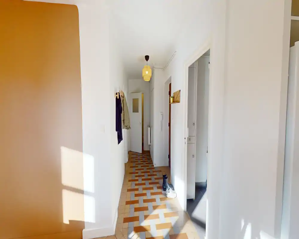 Bright, narrow entrance corridor with patterned tiled floor, wall hooks for coats and natural light from a side window.