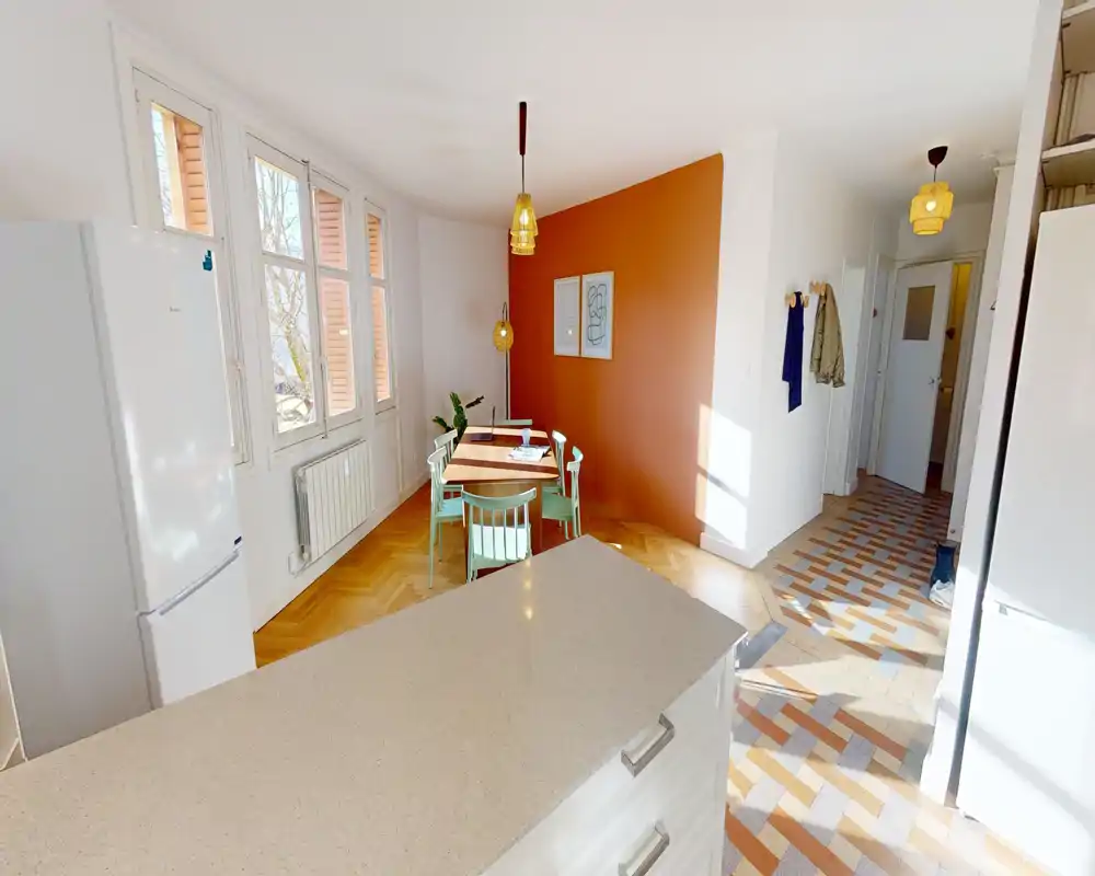 Sunny dining area with a compact wooden table, pastel chairs and warm terracotta accent wall — ideal for cozy meals and natural light.