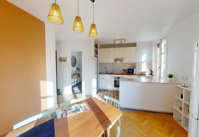 Cuisine ouverte lumineuse avec meubles blancs, plan de travail en bois et une table conviviale baignée de lumière naturelle — idéale pour cuisiner et prendre des repas informels.