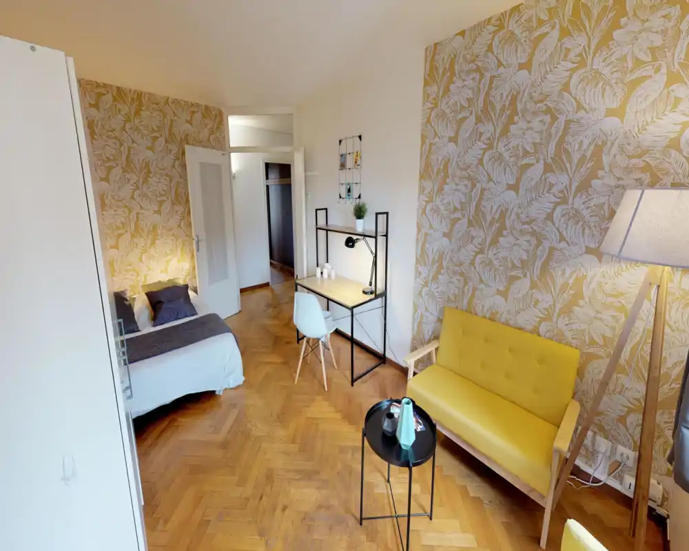 Dormitorio luminoso y con estilo, con cama doble cómoda, suelo de parquet y una zona de trabajo compacta. Papel pintado decorativo y luz cálida crean un ambiente acogedor ideal para alquileres de corta estancia.