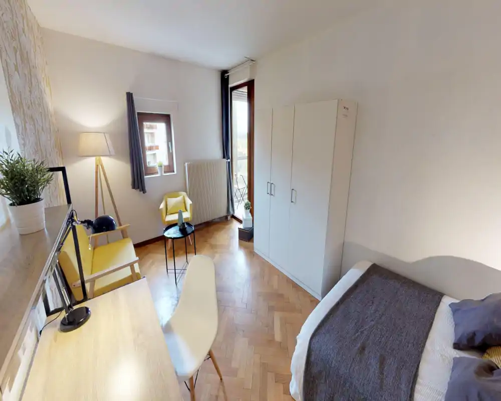 Dormitorio luminoso y acogedor con cama cómoda, armario blanco y una pequeña zona de estar con sillones amarillos, ideal para relajarse o trabajar junto a la ventana.