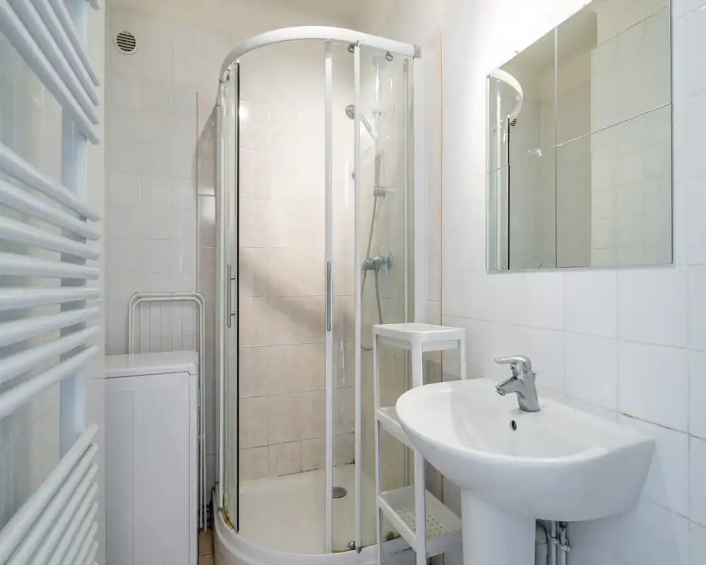 Compact, well-lit bathroom with a corner glass shower, pedestal sink and mirrored cabinet — clean and practical for short stays.