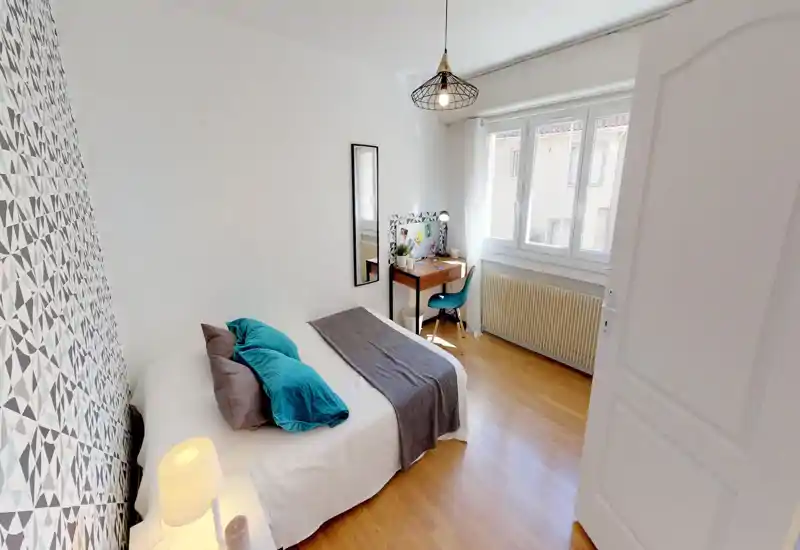 Bright, modern bedroom with a comfortable double bed, decorative patterned accent wall and a small desk by the window — ideal for restful nights and a compact workspace.