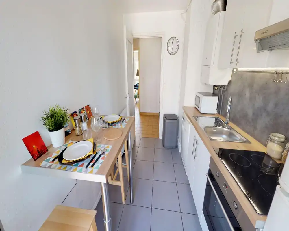 Cucina compatta e moderna con piano in legno, lavello in acciaio, piano cottura elettrico e un piccolo tavolo colazione apparecchiato per due—luminosa, ordinata e ben attrezzata per soggiorni brevi.