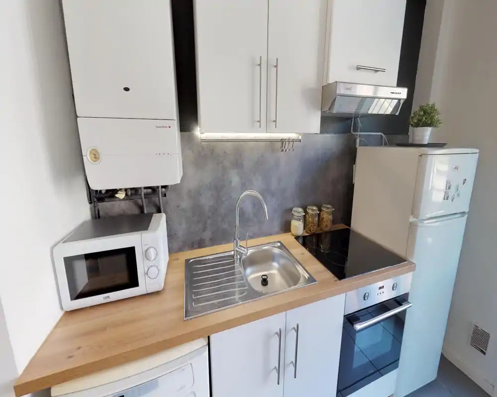 Cucina compatta e moderna con lavello in acciaio, piano cottura elettrico e forno integrato; piano in legno, microonde e frigorifero visibili — luminosa, ordinata e pratica per soggiorni brevi.