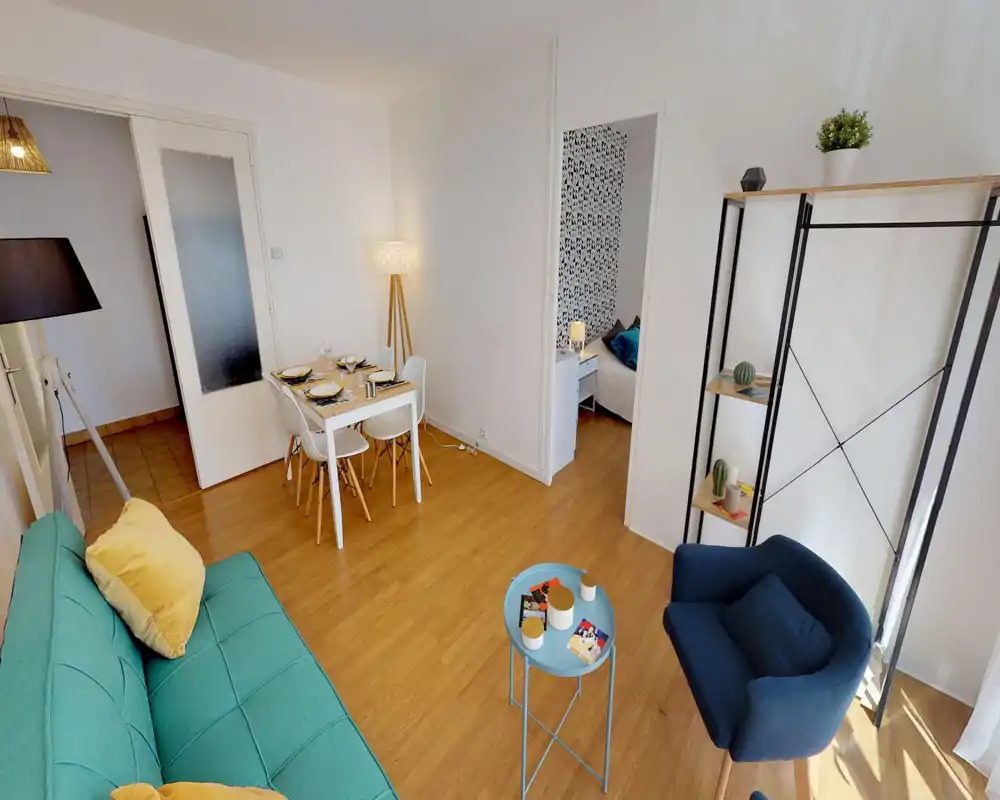 Soggiorno moderno e luminoso con divano turchese, poltrona blu, tavolino e scaffalatura decorativa. Il tavolo da pranzo per quattro e l'illuminazione calda rendono l'ambiente accogliente e di stile.