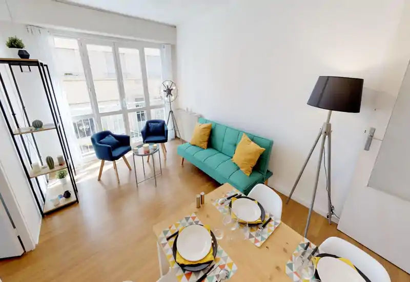 Bright, modern living room with a turquoise sofa, two navy armchairs and a small dining table by large windows providing plenty of natural light.