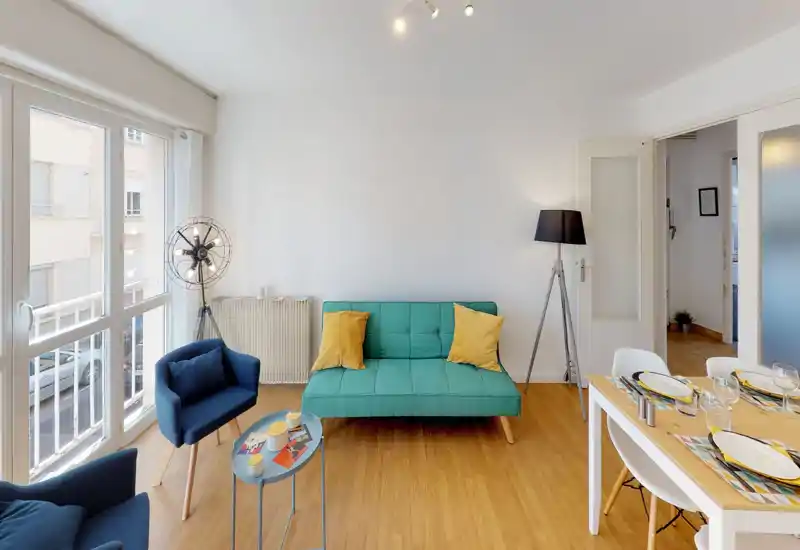 Soggiorno luminoso e moderno con ampie finestre, divano turchese e poltrone confortevoli; pavimento in legno e arredi curati creano un ambiente accogliente ideale per il relax o gli ospiti.