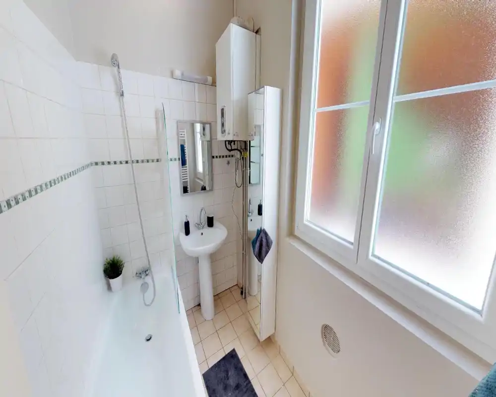 Bright, clean bathroom with a bathtub and handheld shower, pedestal sink, mirror cabinet and frosted window providing privacy and natural light.