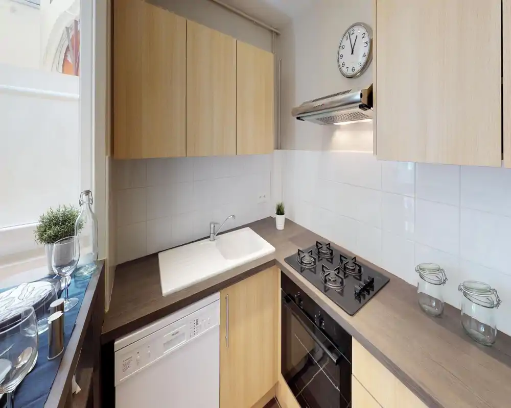 Bright, compact kitchen with wood cabinets, a built-in oven and four-burner gas hob, sink and dishwasher — ideal for efficient meal prep in a small space.