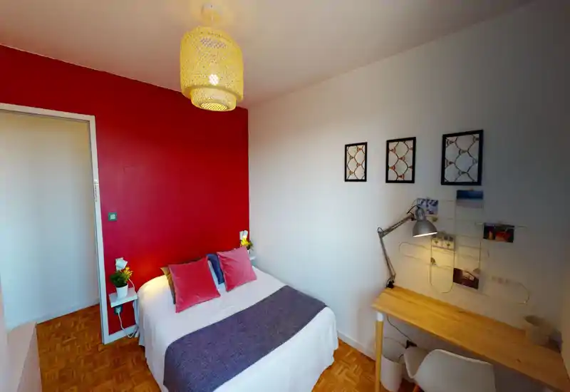 Bright, cozy bedroom with a double bed against a bold red accent wall, bedside shelves and a small wooden desk with a task lamp — ideal for a comfortable stay or short-term rental.