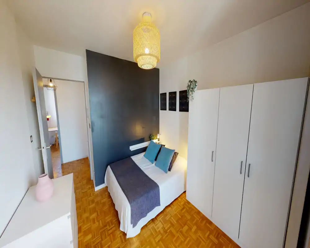 Bright, neatly staged bedroom with a double bed against an accent dark wall, decorative cushions and a large white wardrobe for storage.