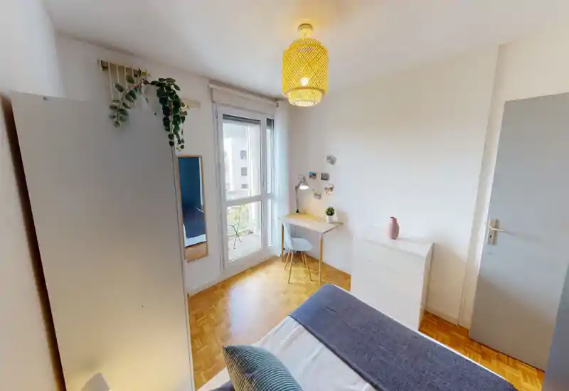 Bright, tidy bedroom with a comfortable bed in the foreground, a small desk by the window and a chest of drawers — ideal for a single occupant or student.