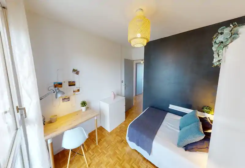 Bright, well-styled single bedroom with a comfortable bed against a dark accent wall, a wooden desk by the window, and tasteful decorative touches including cushions, plants and soft lighting.