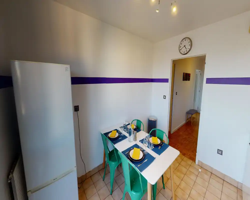 Bright, tidy kitchen with a small dining table set for four, teal chairs and a freestanding refrigerator – ideal for a compact apartment.