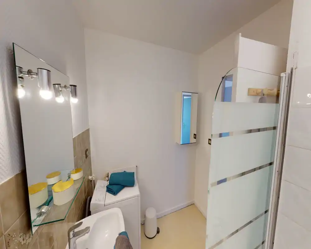 Bright, clean bathroom with a sink, mirror with lights, a washing machine, and a glass shower screen with frosted stripes.