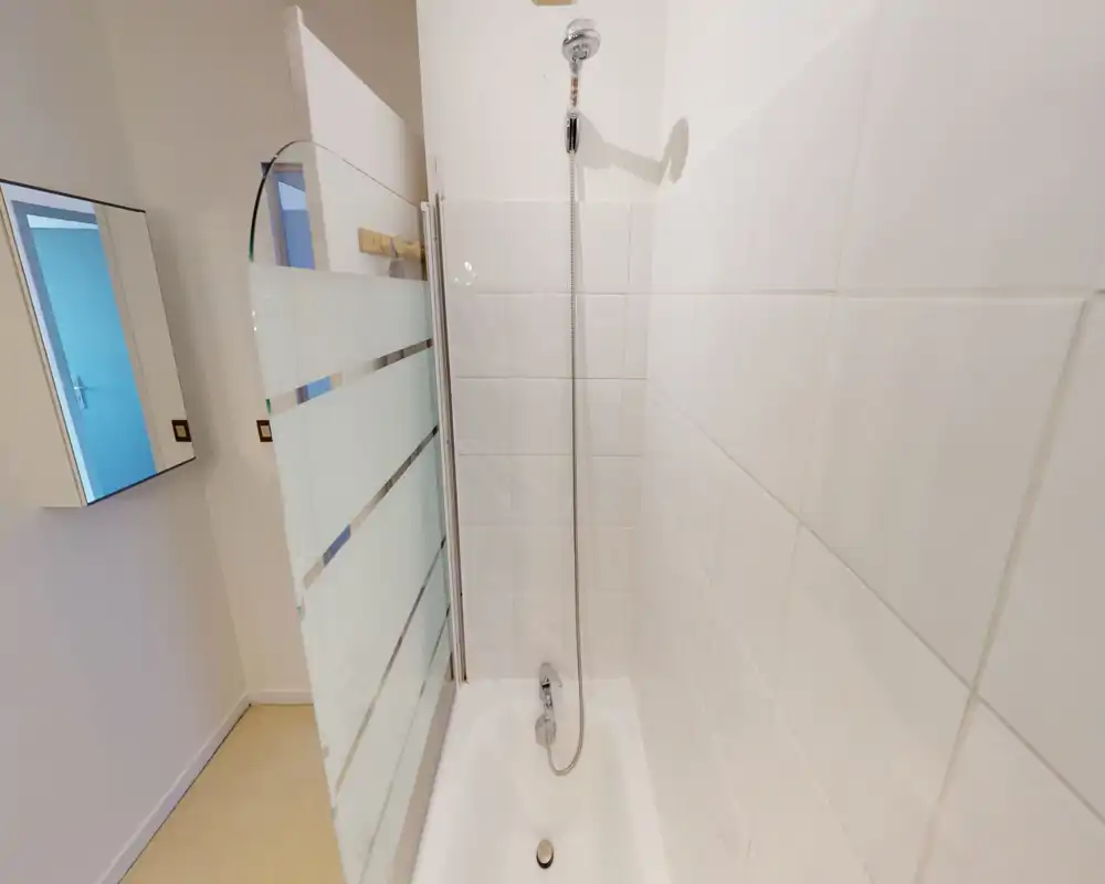 Compact bathroom with a tiled shower-bathtub, wall-mounted shower head and a frosted glass shower screen. Clean white tiles and a simple, functional layout ideal for a short-stay rental.