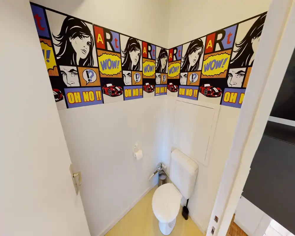 Small, well-lit bathroom with a wall-mounted cistern toilet and comic-style wallpaper border; clean and simple layout ideal for a guest WC.