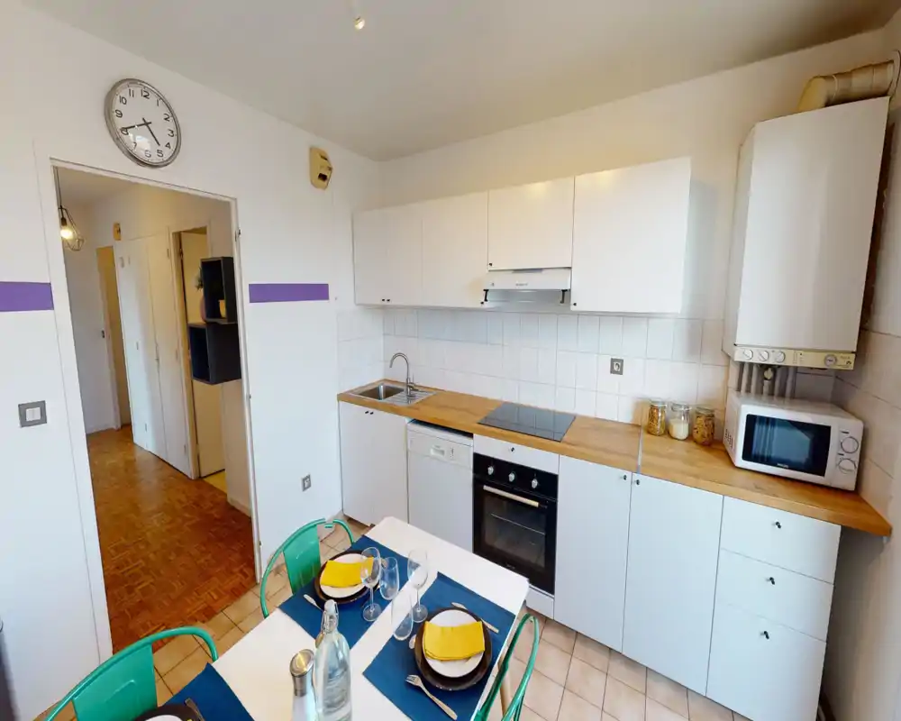 Bright, compact kitchen with white cabinets, wooden countertops, electric oven and hob, a sink, microwave and a set dining table — ideal for a small apartment.