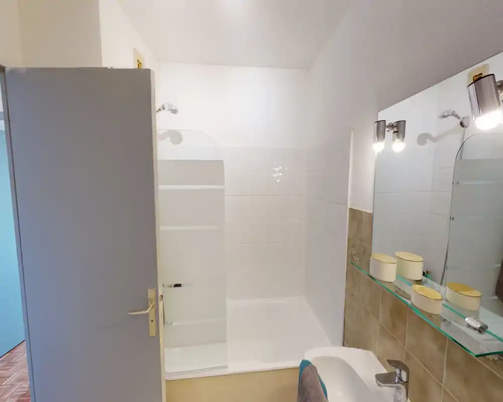 Clean, compact bathroom with a shower-tub combo, tiled walls and a wall-mounted mirror with lights above the sink.