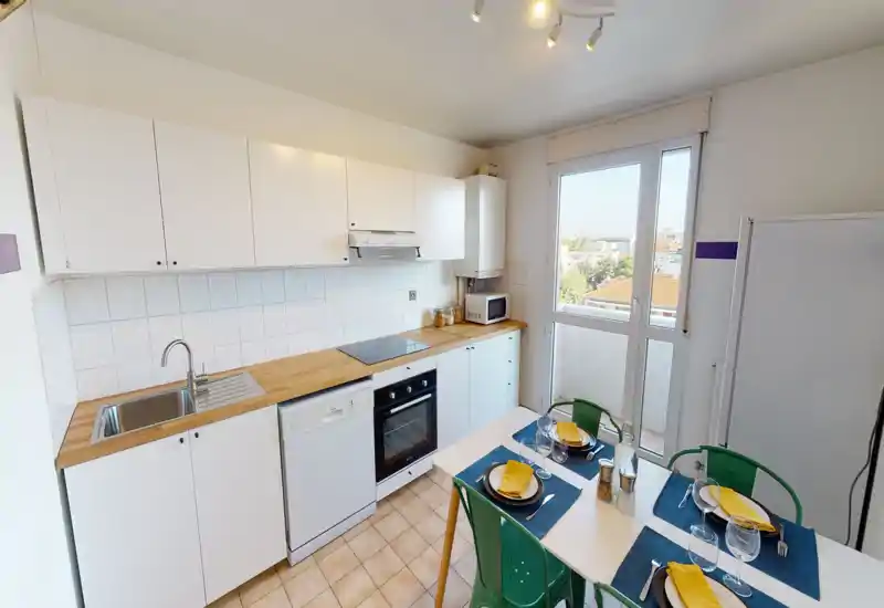 Bright, modern kitchen with white cabinets, wooden countertops, built-in oven and dishwasher, plus a small dining table set for four. Large window provides natural light and a pleasant view.