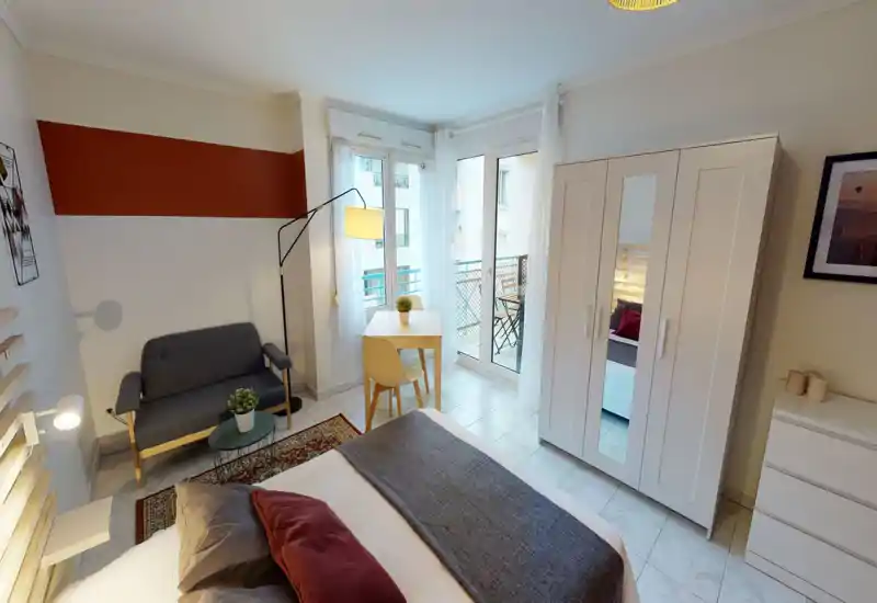 Camera da letto luminosa e moderna con letto comodo, tessili accoglienti e una piccola zona salotto. Ampia finestra e porta sul balcone che garantiscono molta luce naturale e un tavolo per pranzo/lavoro.
