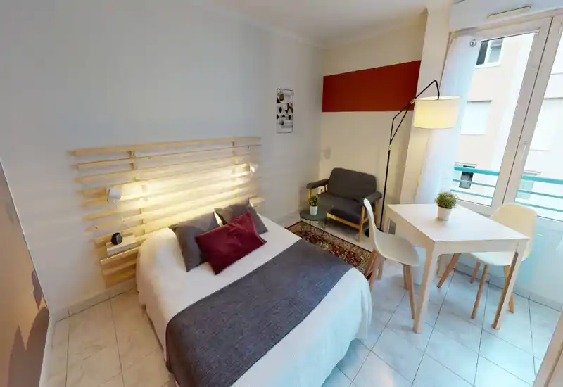 Camera da letto luminosa e ben arredata con letto matrimoniale, cuscini decorativi e una testiera in listelli di legno. La stanza dispone di un piccolo angolo relax, tavolo e sedie vicino a una grande finestra che illumina l'ambiente.