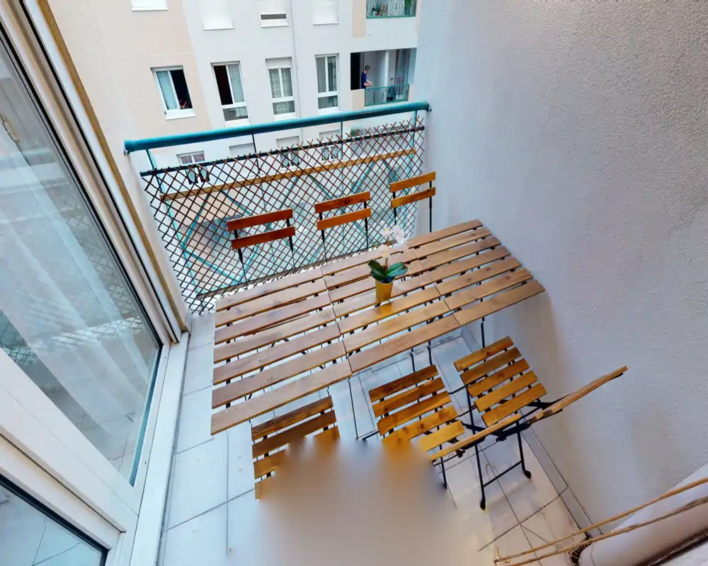 Balcon étroit et ensoleillé avec une table bistro en bois et une petite plante en pot — idéal pour un café du matin en appartement urbain.