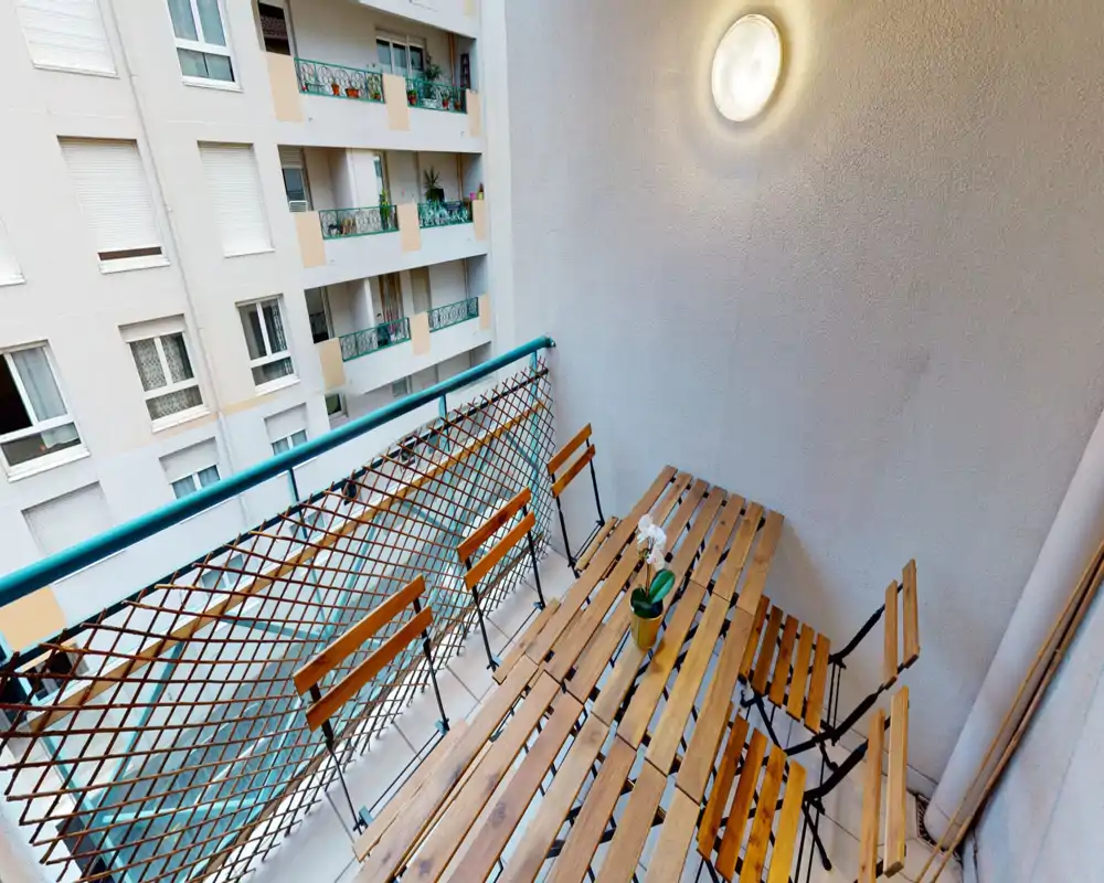 Petit balcon ensoleillé avec table bistrot en bois et chaises pliantes, parfait pour un café matinier ou un petit repas.