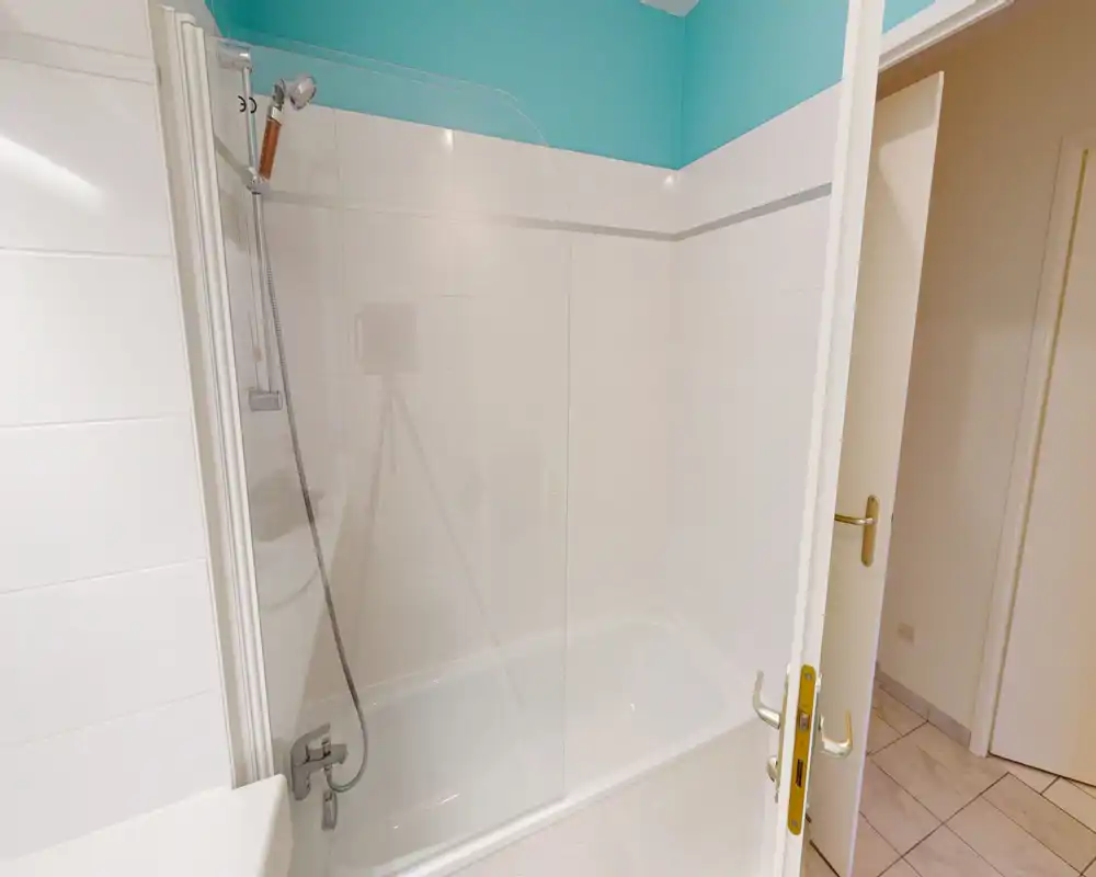 Salle de bains lumineuse et propre avec baignoire-douche, paroi de verre et carrelage — agencement fonctionnel et soigné.
