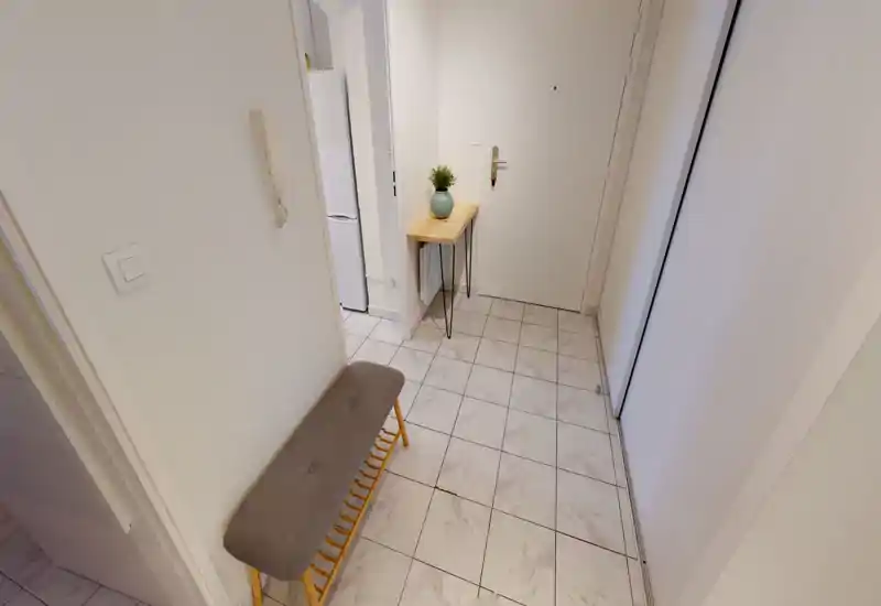Entrée lumineuse et soignée avec sol carrelé, petite table console en bois avec plante et banc rembourré — espace d'accueil pratique et plaisant.