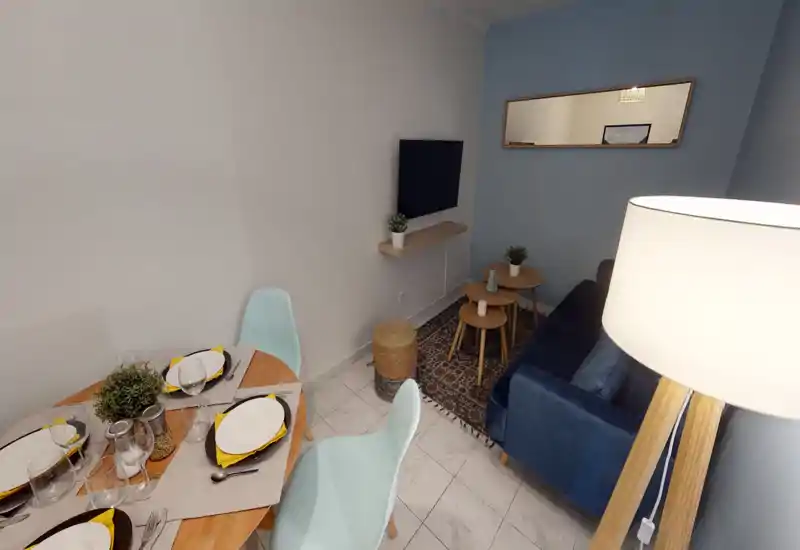Espace de vie compact et stylé avec canapé bleu, tables basses gigognes et TV murale ; une table à manger pour quatre personnes adjacente crée une disposition ouverte et accueillante.