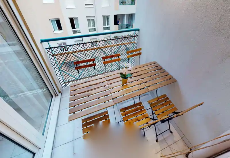Balcon étroit et ensoleillé avec une table bistro en bois et une petite plante en pot — idéal pour un café du matin en appartement urbain.