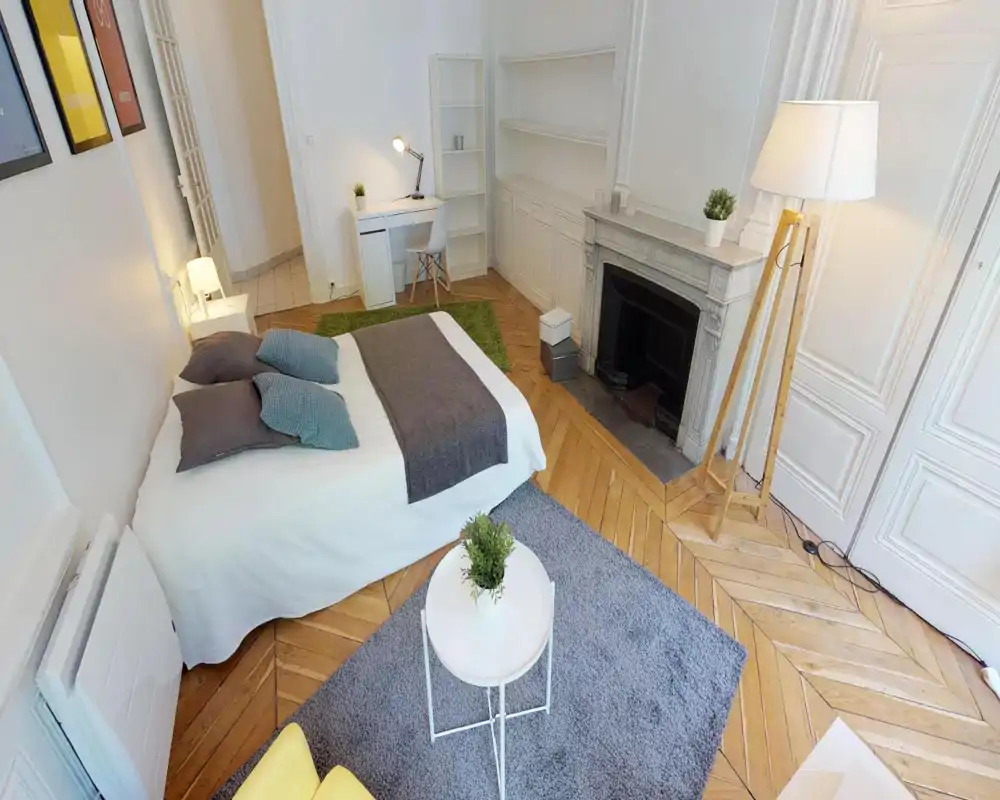 Dormitorio luminoso y con estilo con cama doble grande, cojines decorativos, escritorio y una elegante chimenea; el parqué en espiga y las alfombras aportan calidez.