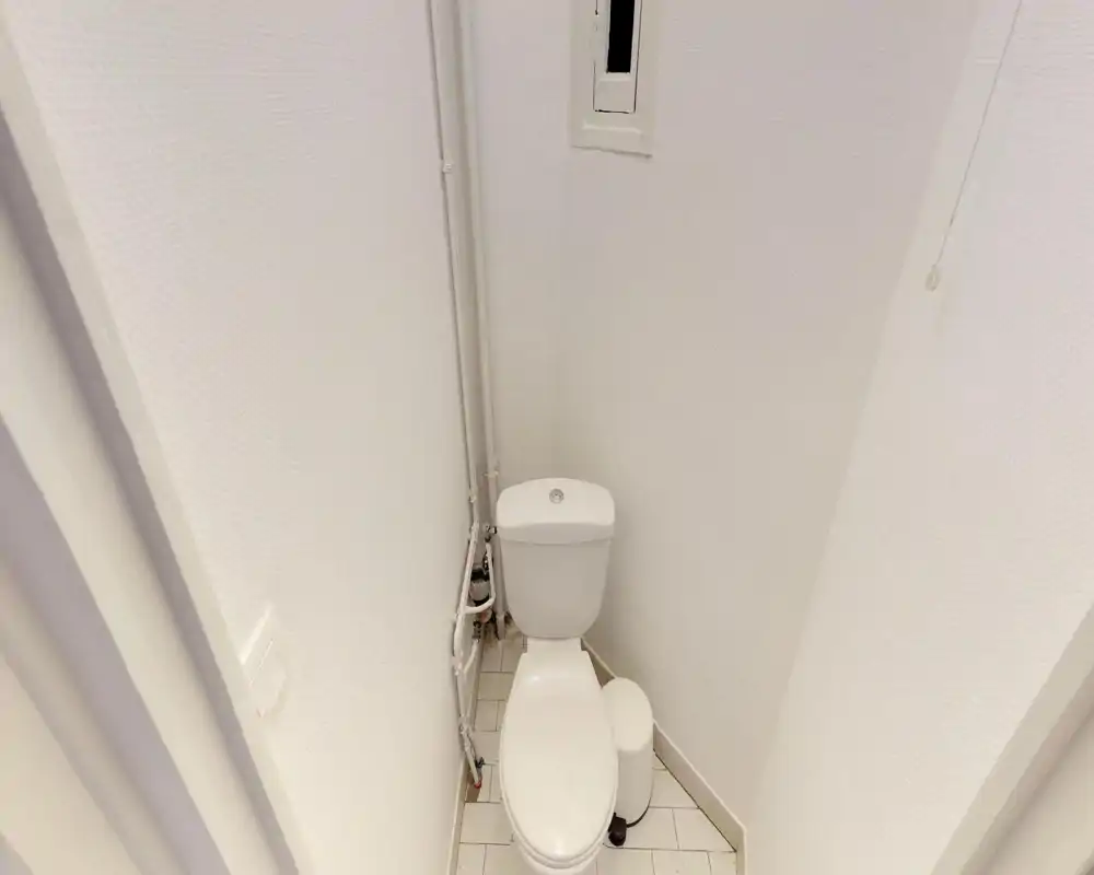 Compact, clean small bathroom with a white toilet, exposed plumbing and tiled floor—well-lit and simply finished.