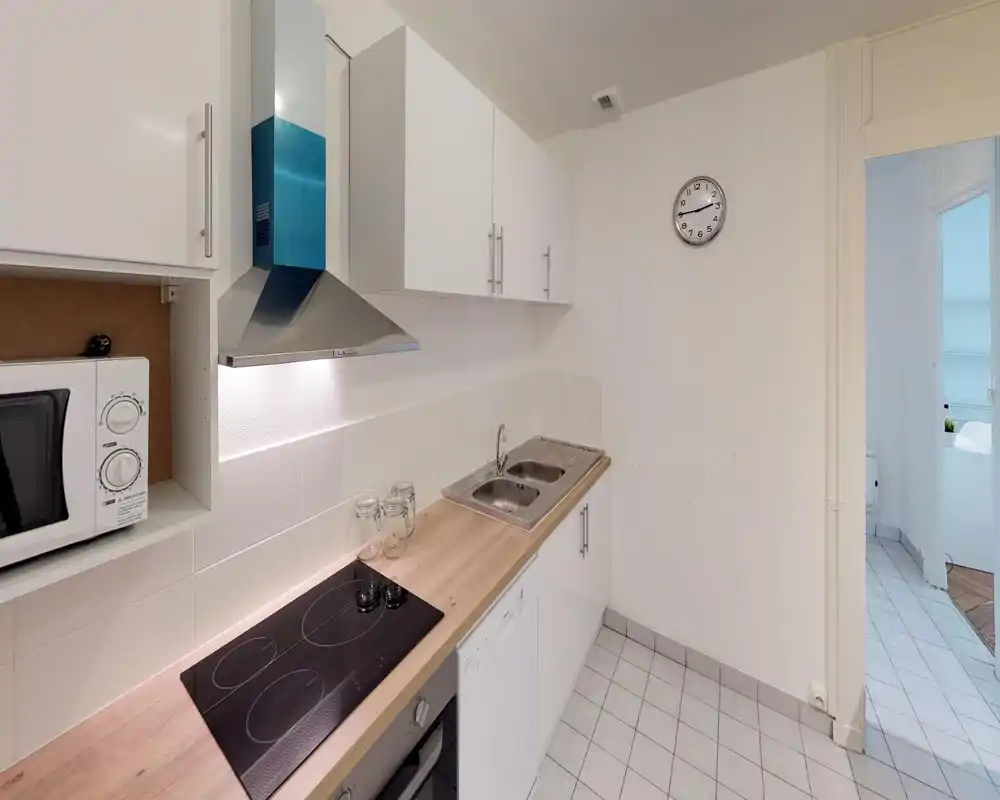 Compact modern kitchen with a ceramic cooktop, stainless sink, white cabinets and wooden countertop. Bright, clean and efficiently arranged for city apartment cooking.