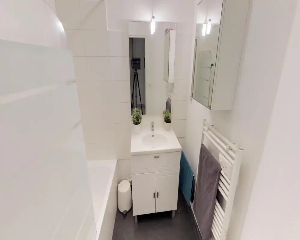 Small modern bathroom with a white sink cabinet, mirror, towel radiator and a bathtub with frosted glass panel. Bright, clean and simply styled — suitable for rental listing photos.