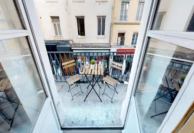 Small balcony with outdoor metal table and chairs; image is visually distorted but shows a narrow terrace space with a railing.