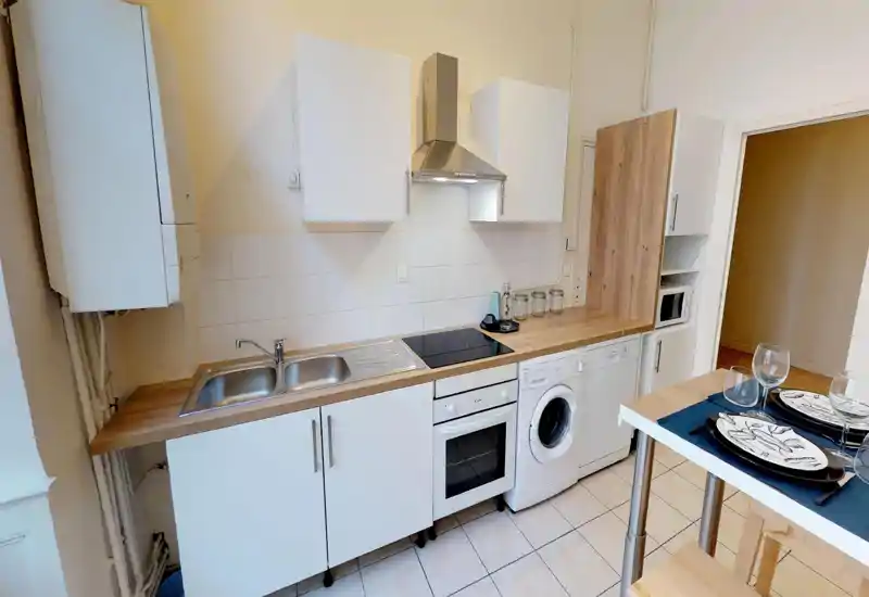 Cucina compatta e moderna con piano in legno, mobili bianchi, forno incassato e lavatrice; ambiente ordinato e ben illuminato ideale per un piccolo appartamento.