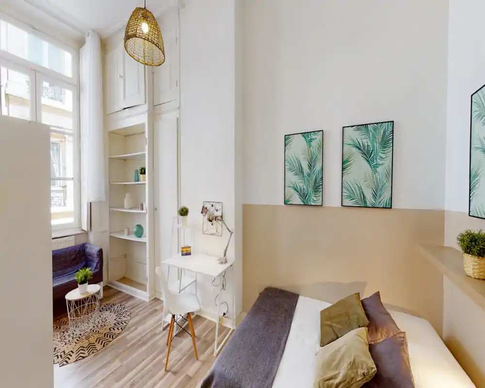 Bright, well-staged bedroom with a comfortable double bed, cozy pillows and tasteful botanical wall art. The room features a small workspace, natural light from a large window and coordinated neutral tones.