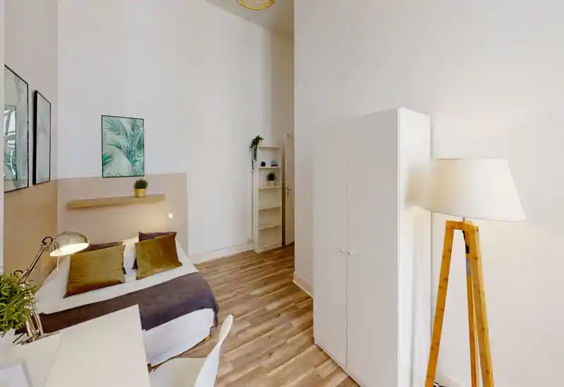 Bright, stylish bedroom with a comfortable double bed, decorative cushions, a desk area and modern storage. Tall ceilings and warm wooden flooring create an airy, welcoming atmosphere.